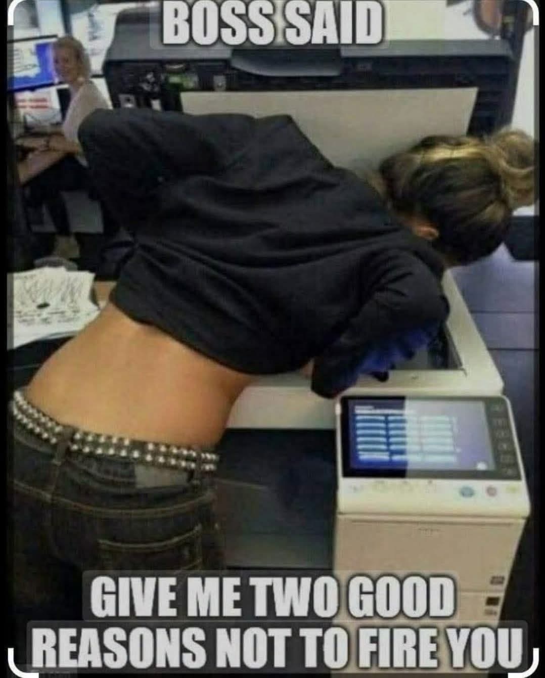 Woman in a dark hoodie and jeans leaning over an office photocopier, with meme text reading "Boss said give me two good reasons not to fire you"
